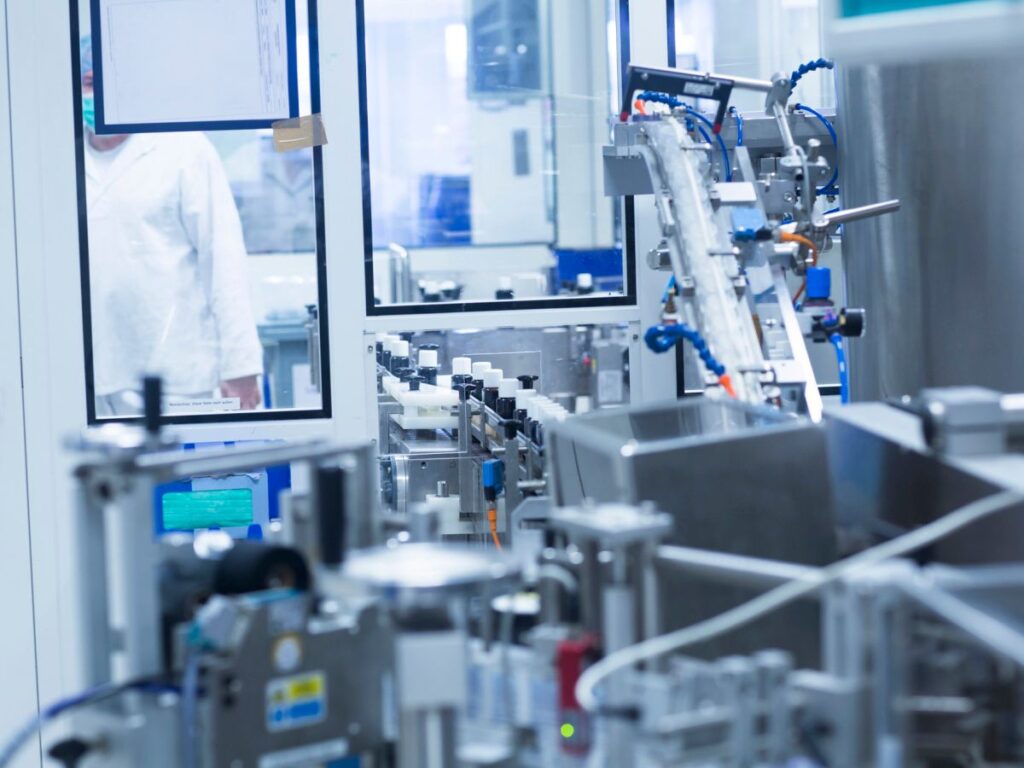 Detailní pohled na automatizovanou plnicí linku v čistých prostorách farmaceutické výroby.