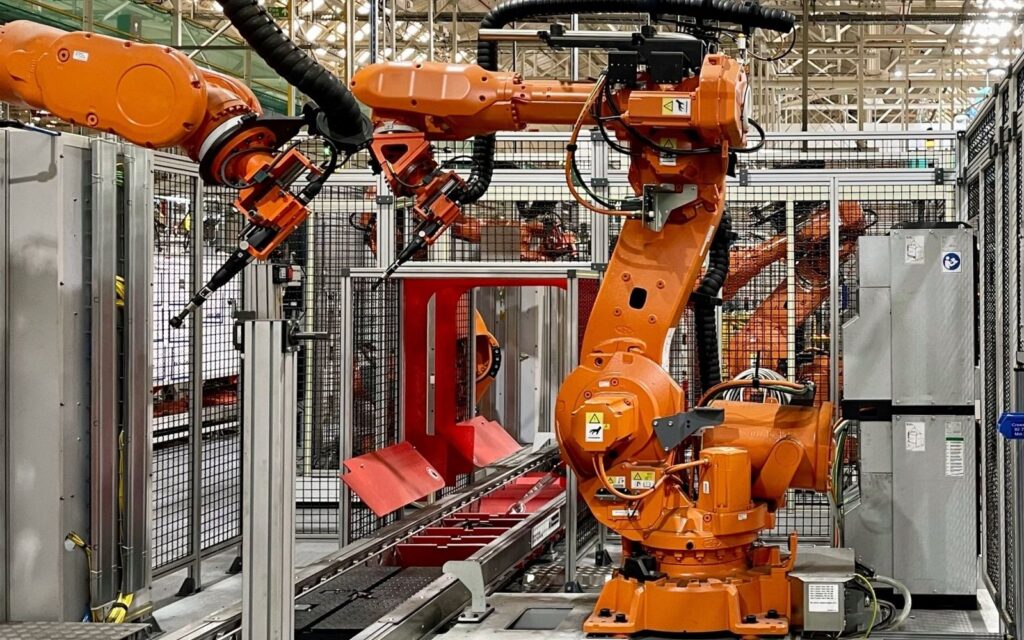 Plně automatizované průmyslové robotické stanoviště s oranžovým ramenem v kryté buňce.
